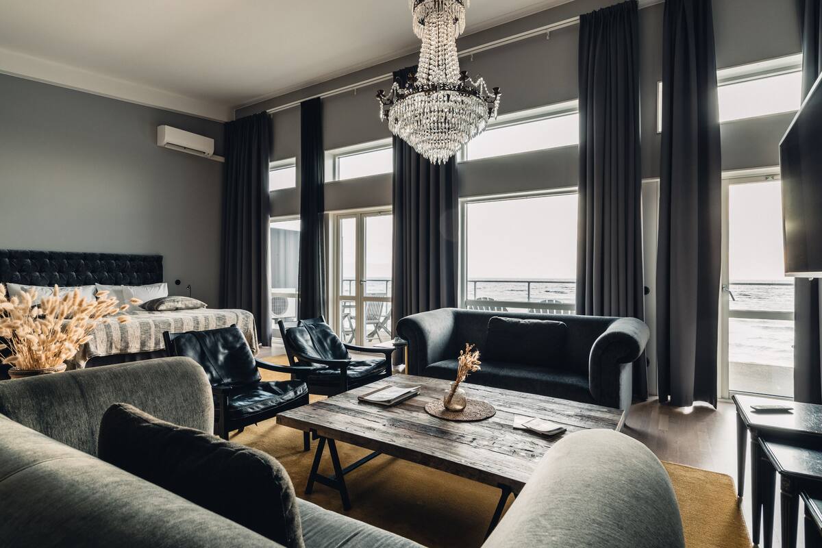 Habitación de hotel moderna con una cama grande, un sofá, una mesa de centro y vistas al mar.