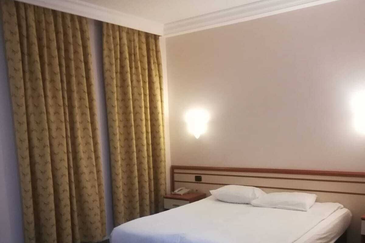 A hotel room with a bed, a nightstand, a lamp, and curtains.