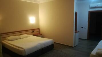 Habitación de hotel con cama, mesita de noche y aire acondicionado instalado en la pared.
