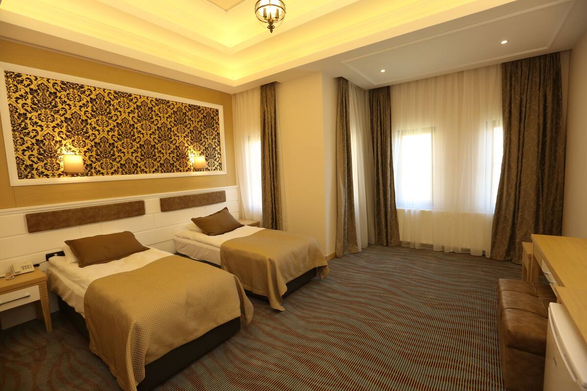 A hotel room with two beds, a desk, a sofa, a patterned wall, and a large window with curtains.