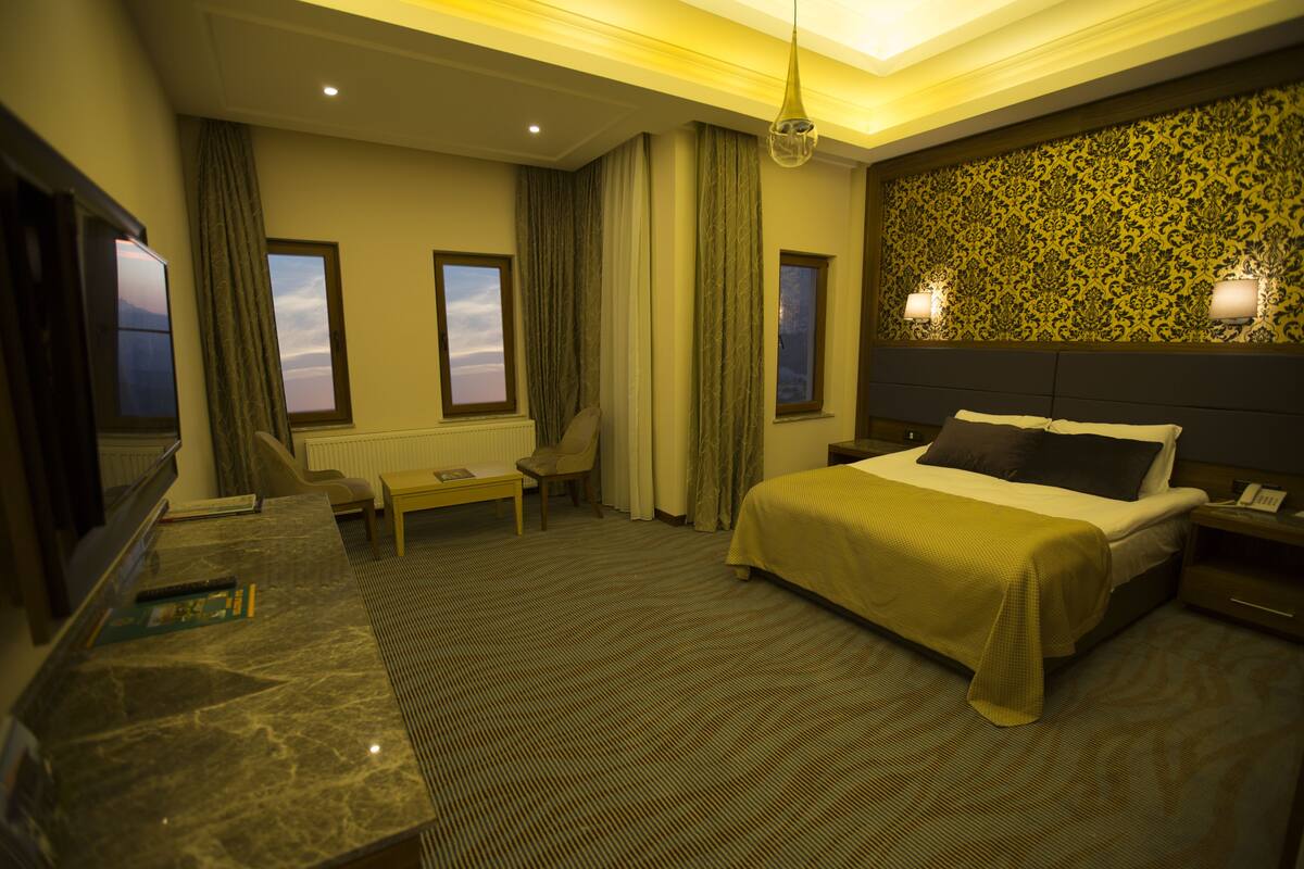 A hotel room with a bed, bedside table, lamp, chair, and a desk with a computer.