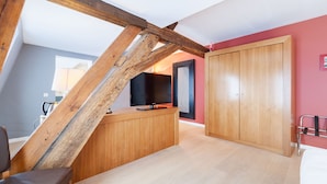A room with a sloped ceiling, a wooden desk, a television, and a wardrobe.