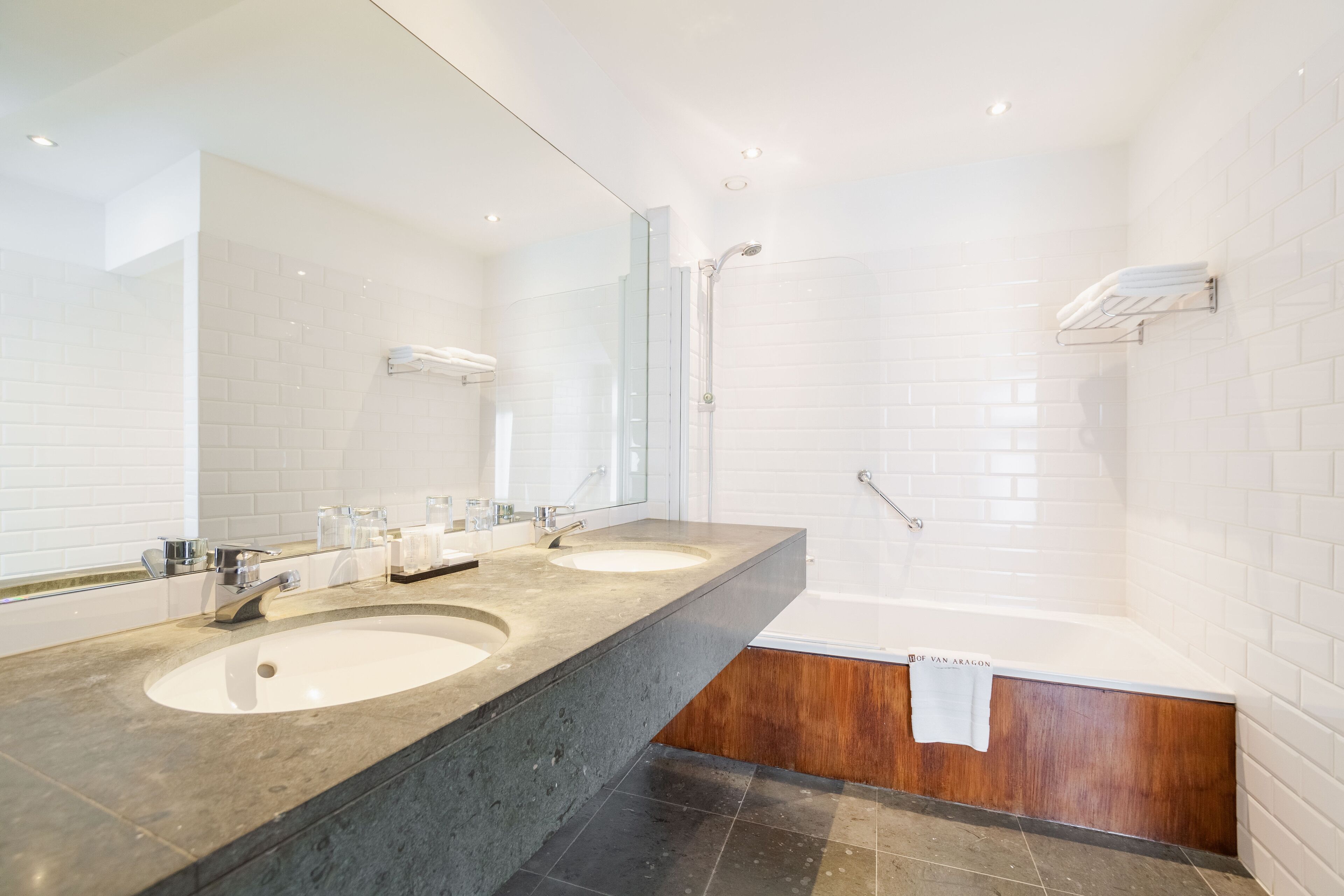 A modern bathroom with two sinks, a large mirror, a shower, and a wooden vanity.