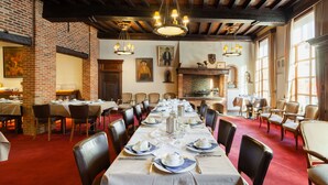 A long dining table set for a meal in a room with brick walls, wooden beams, and chandeliers.