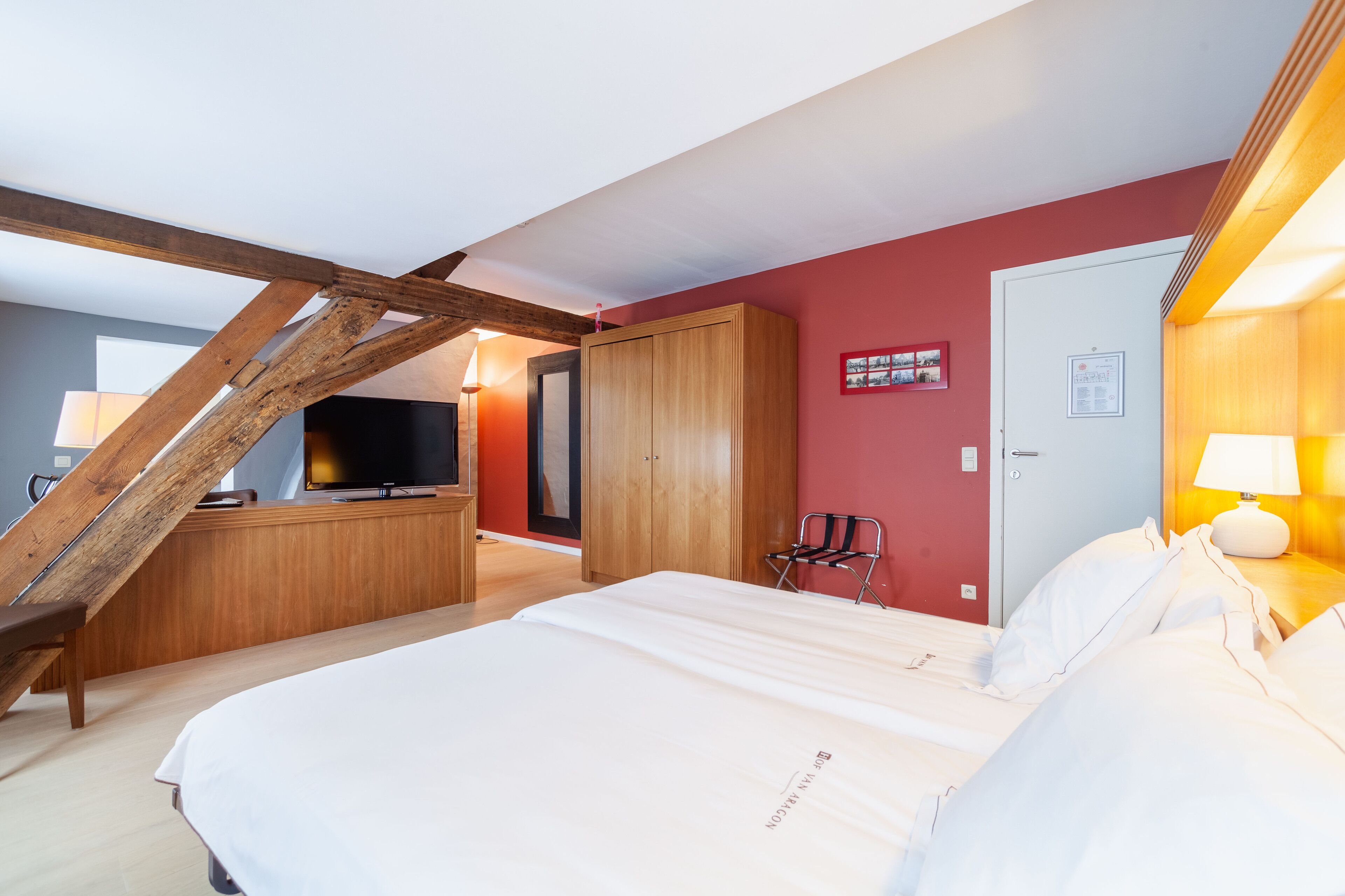 A bedroom with a large bed, wooden wardrobe, and a TV in the corner.