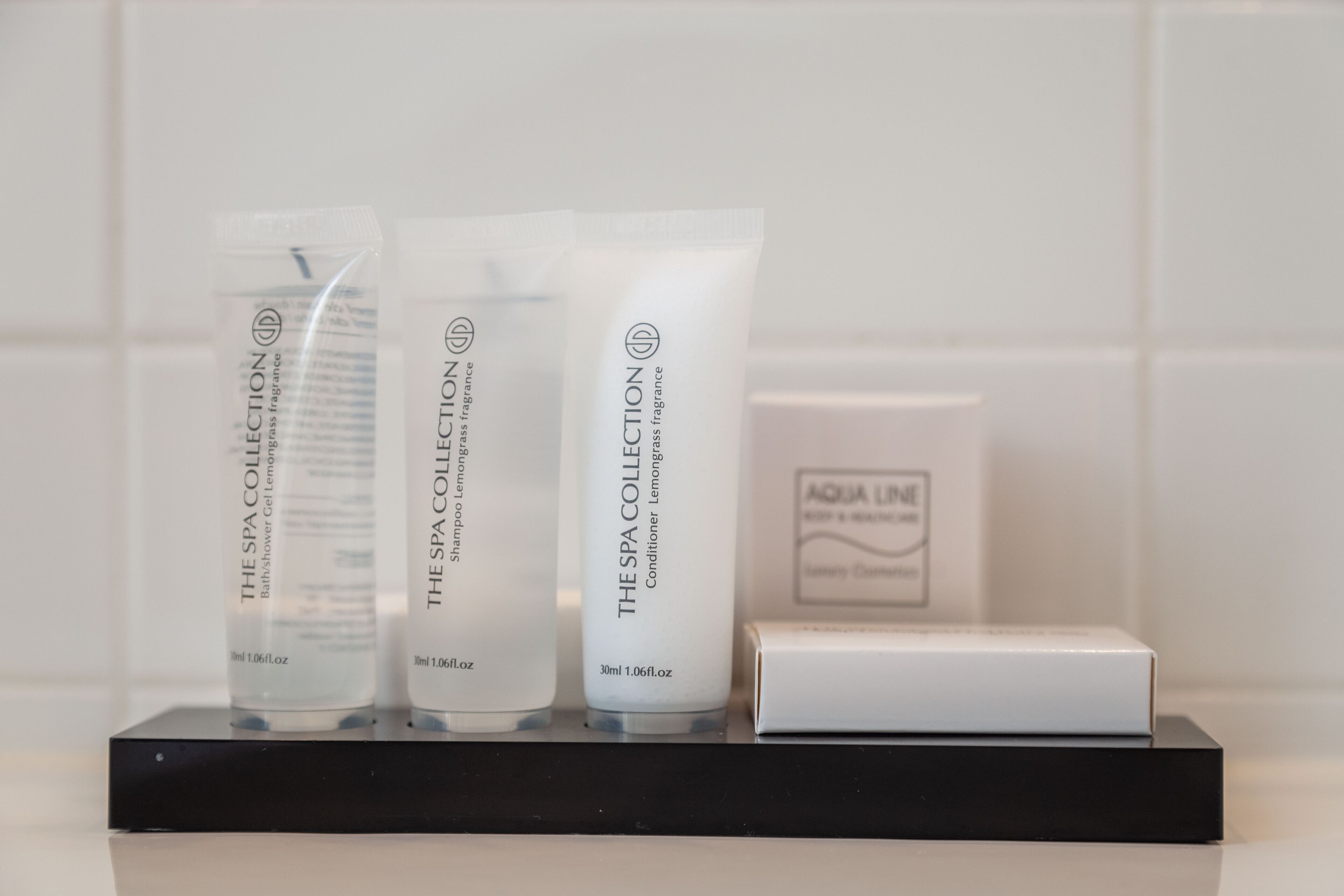 Three spa collection products on a black tray against a white tiled wall.