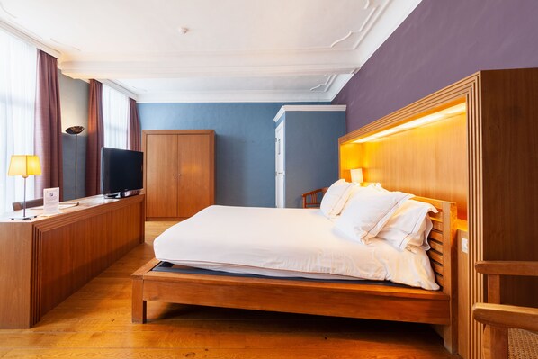 Una habitación de hotel con una cama de madera, un escritorio con televisor y un armario.