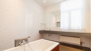 Een moderne badkamer met witte metrotegels, een groot bad, een wastafelmeubel met spiegel en een raam met dunne gordijnen.