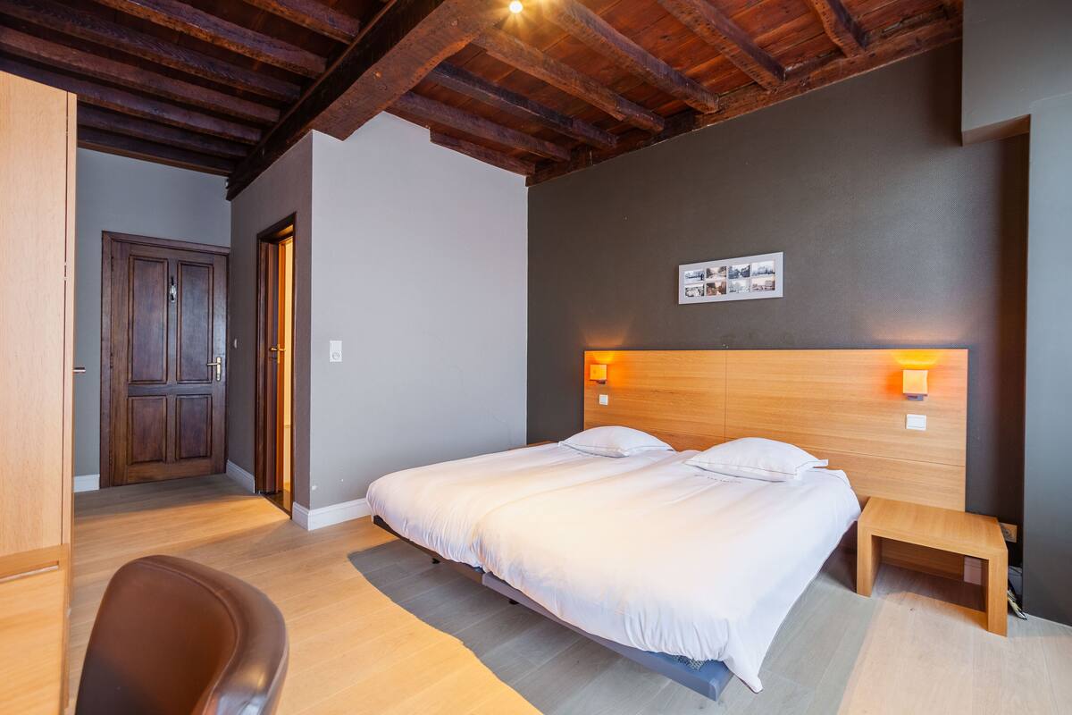 A bedroom with a wooden ceiling, a bed with white bedding, a bedside table, and a wall-mounted light.