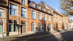 A row of brick buildings with multiple windows and doors, a cobblestone street, and a clear blue sky.