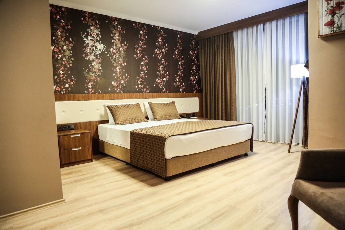 A hotel room with a bed, a nightstand, a chair, a lamp, and a window with curtains.