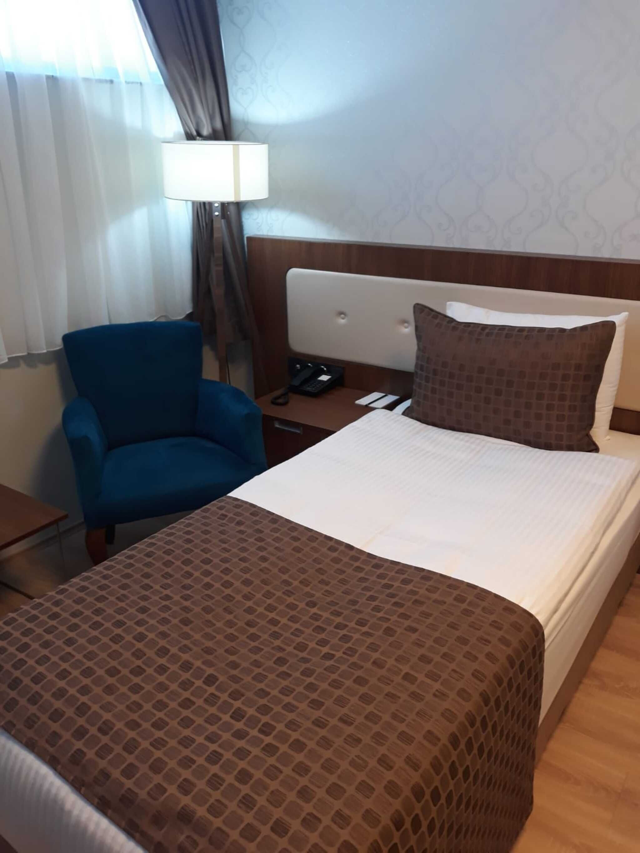 Ein Hotelzimmer mit Bett, Schreibtisch, Stuhl, Lampe und Telefon.