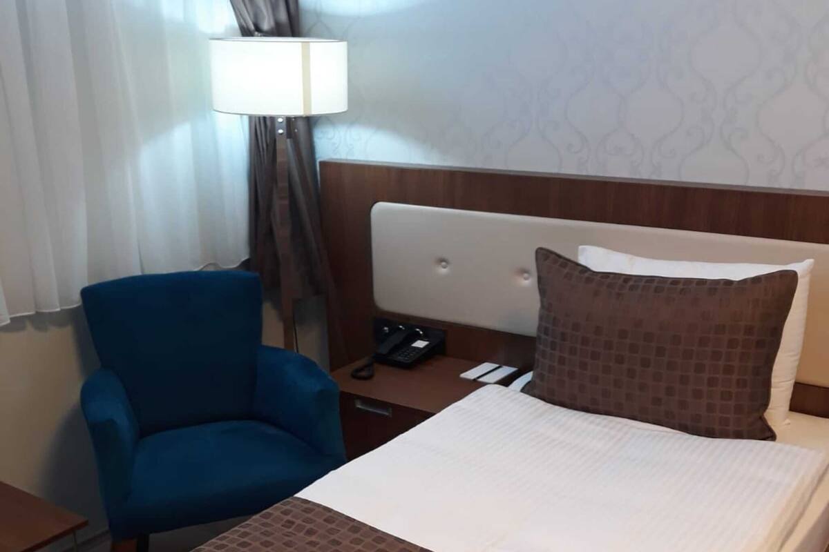 A hotel room with a bed, a desk, a chair, a lamp, and a telephone.