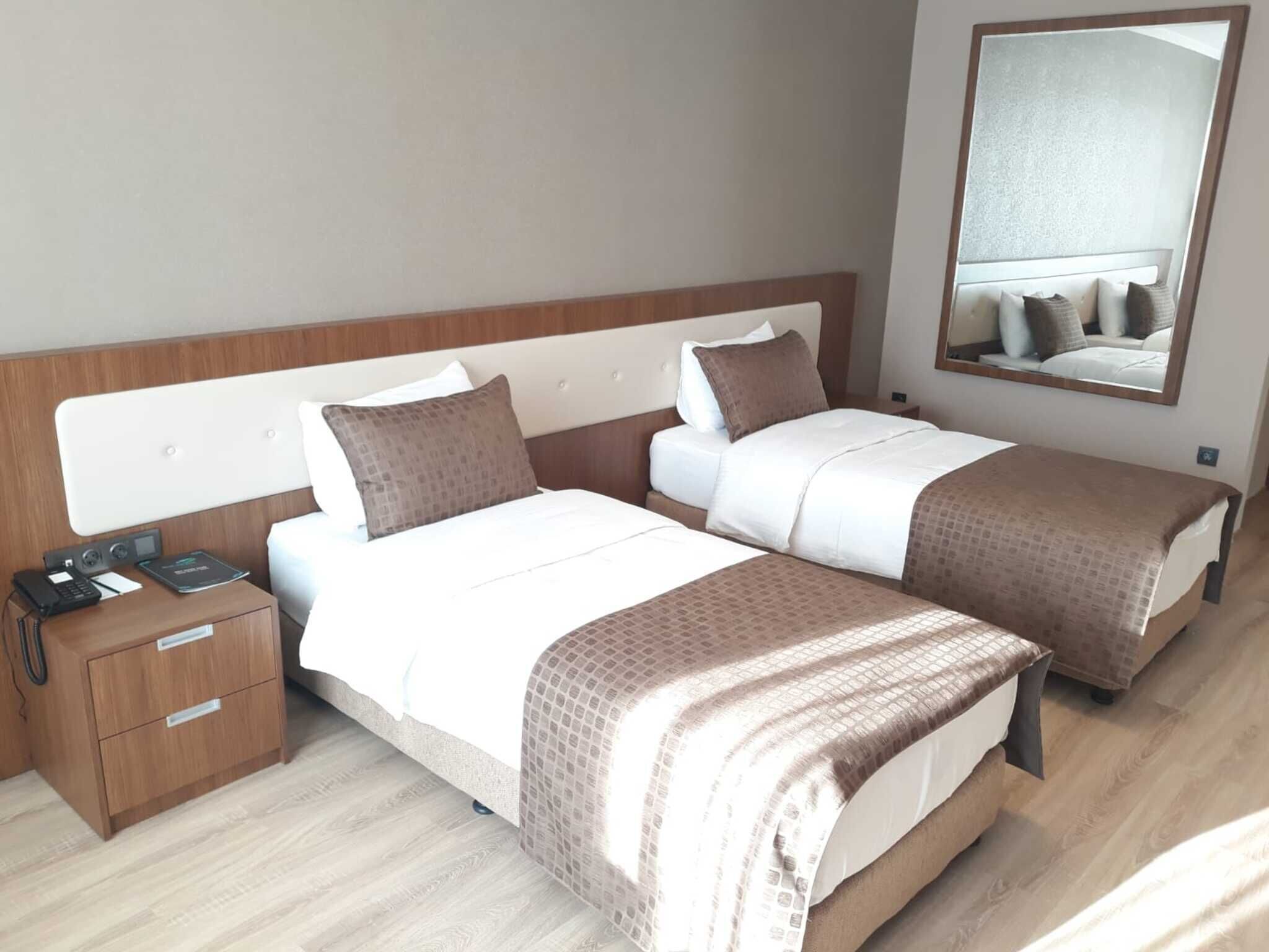 Ein Hotelzimmer mit zwei Betten, einem Nachttisch mit Telefon und Ladegerät, einem Spiegel und Holzboden.