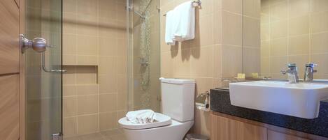 A modern bathroom with a glass shower enclosure, a white toilet, a sink with a black countertop, and a trash can.