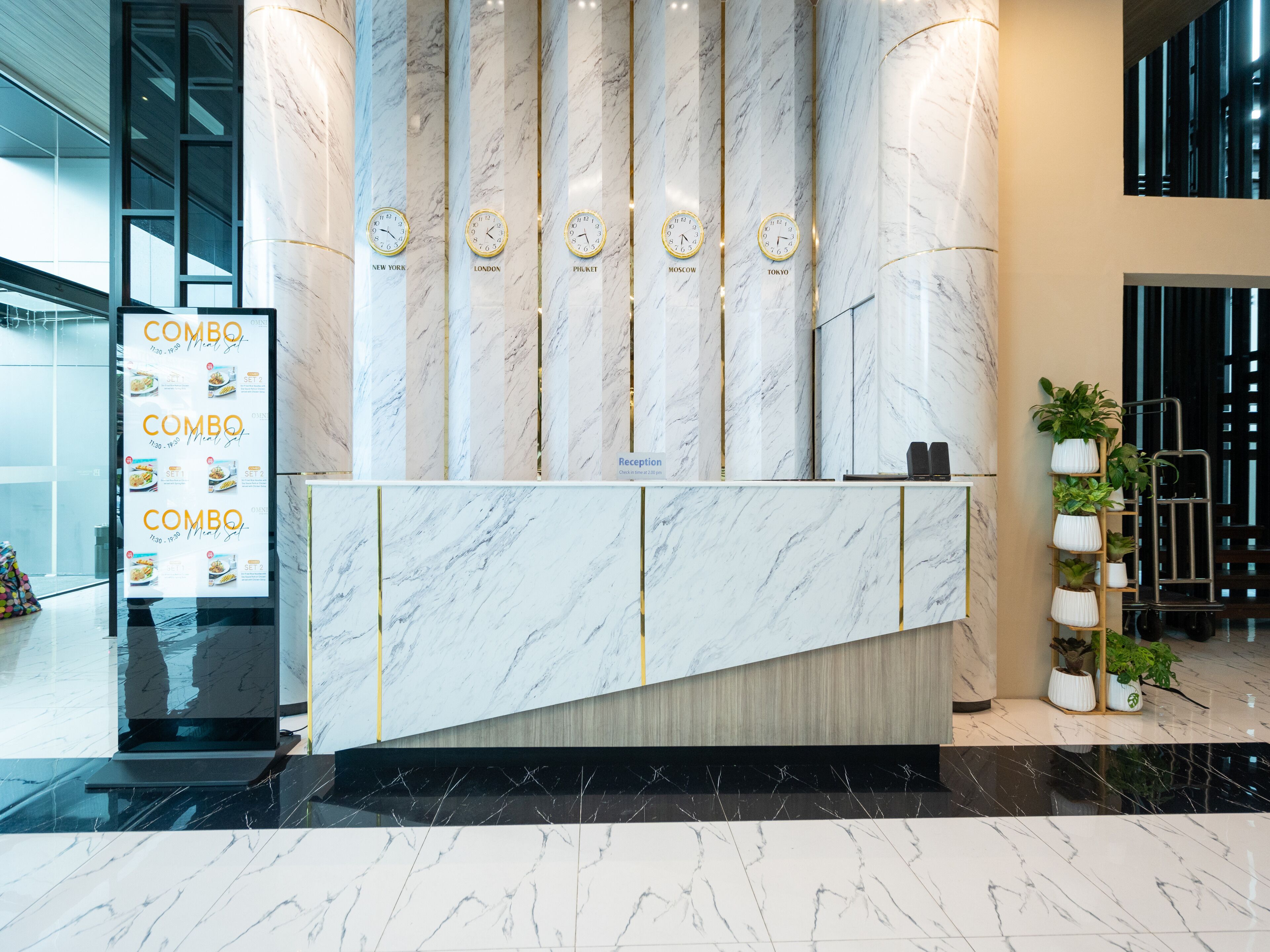A reception desk with a marble finish, clocks indicating different time zones, and a menu board to the left.
