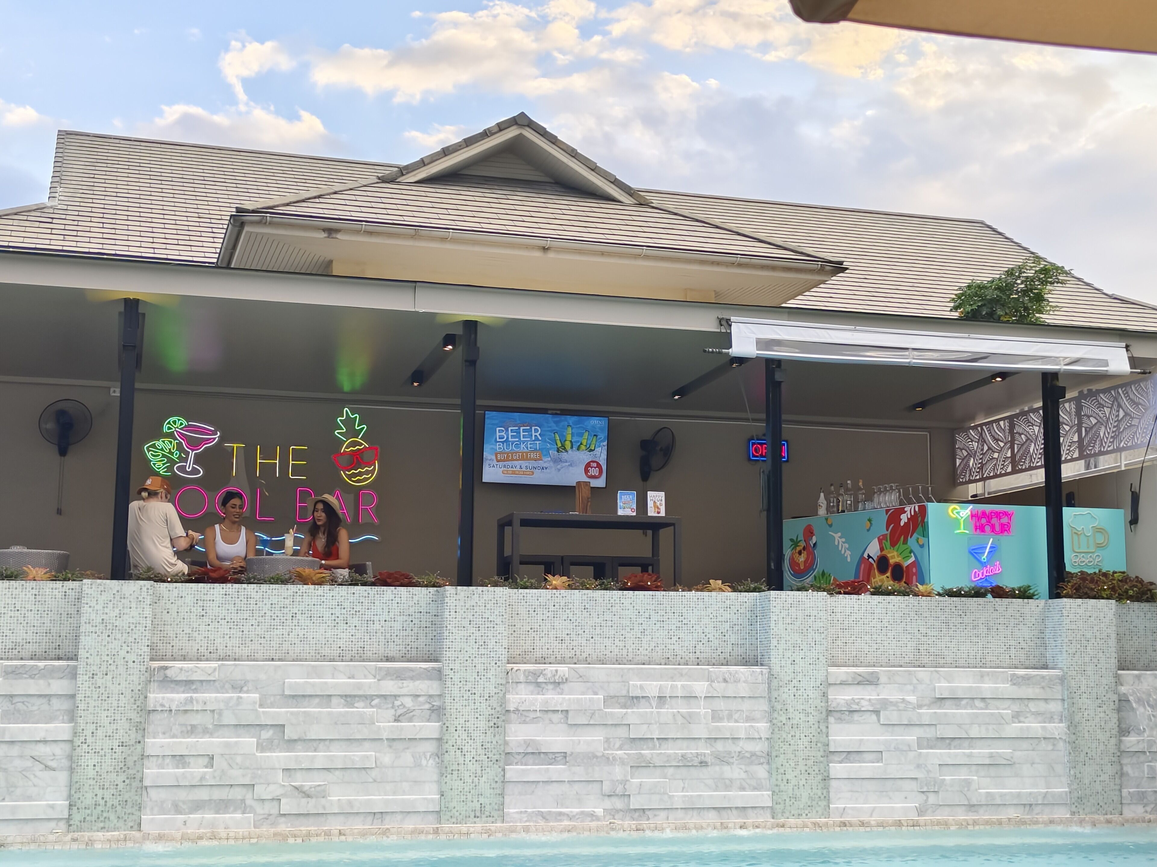 A bar with a neon sign, outdoor seating, and a pool.