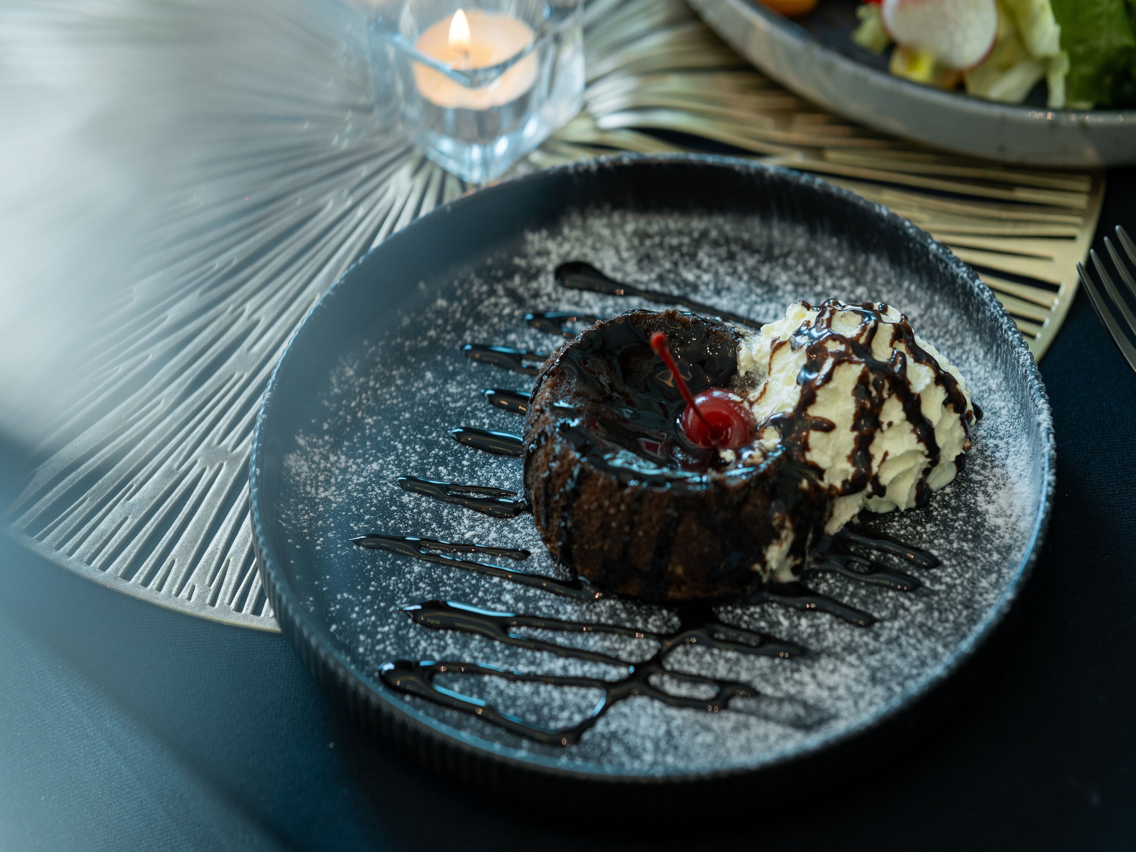 A dessert on a plate with a candle in the background.