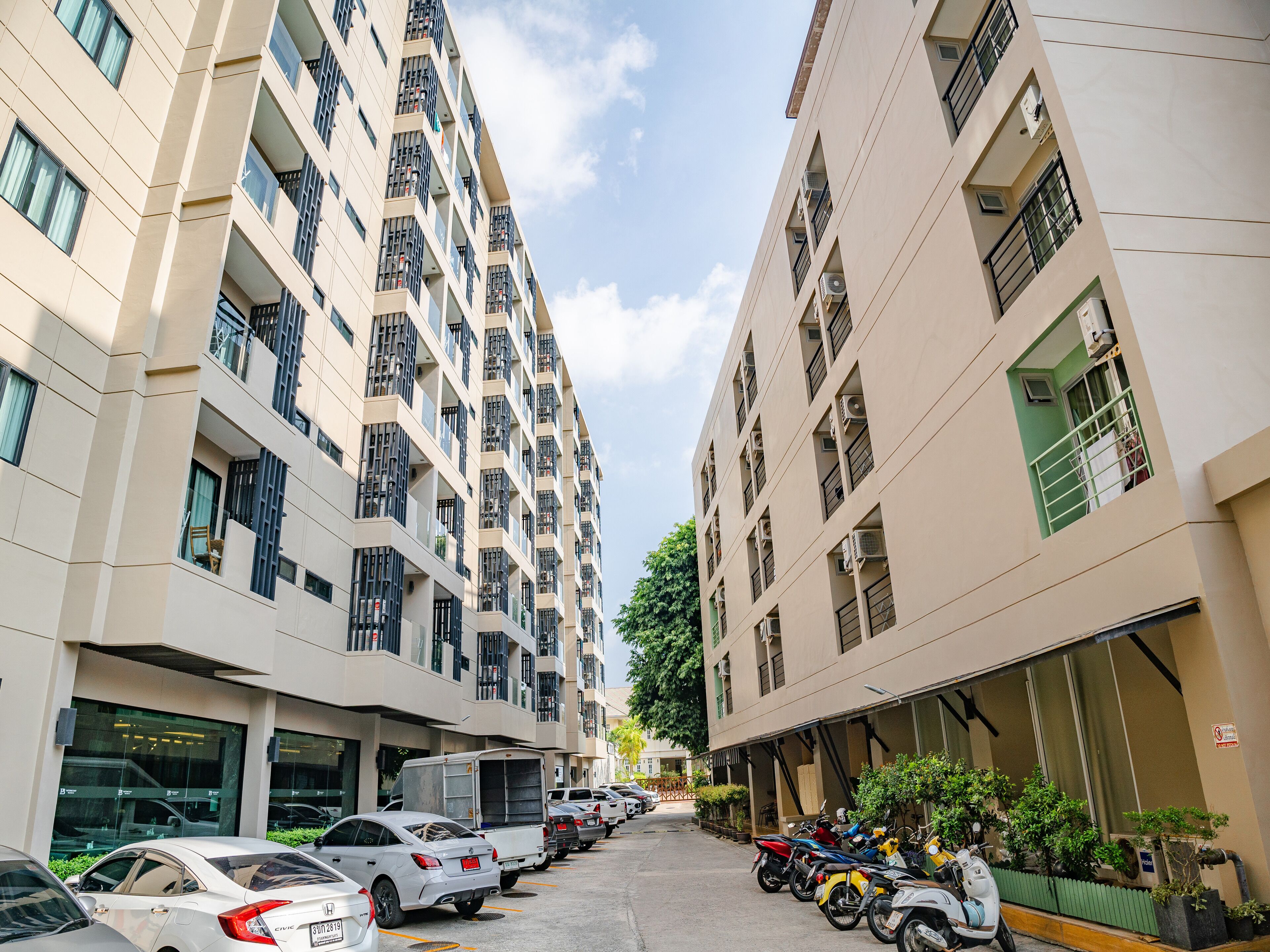 A multi-story residential building with balconies, parked cars, and motorcycles.