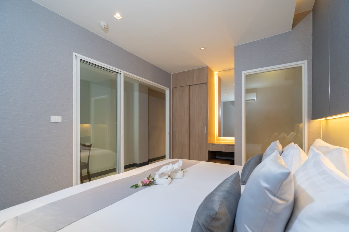 A modern bedroom with a large bed, a sliding glass door leading to a bathroom, and a mirror above the bed.