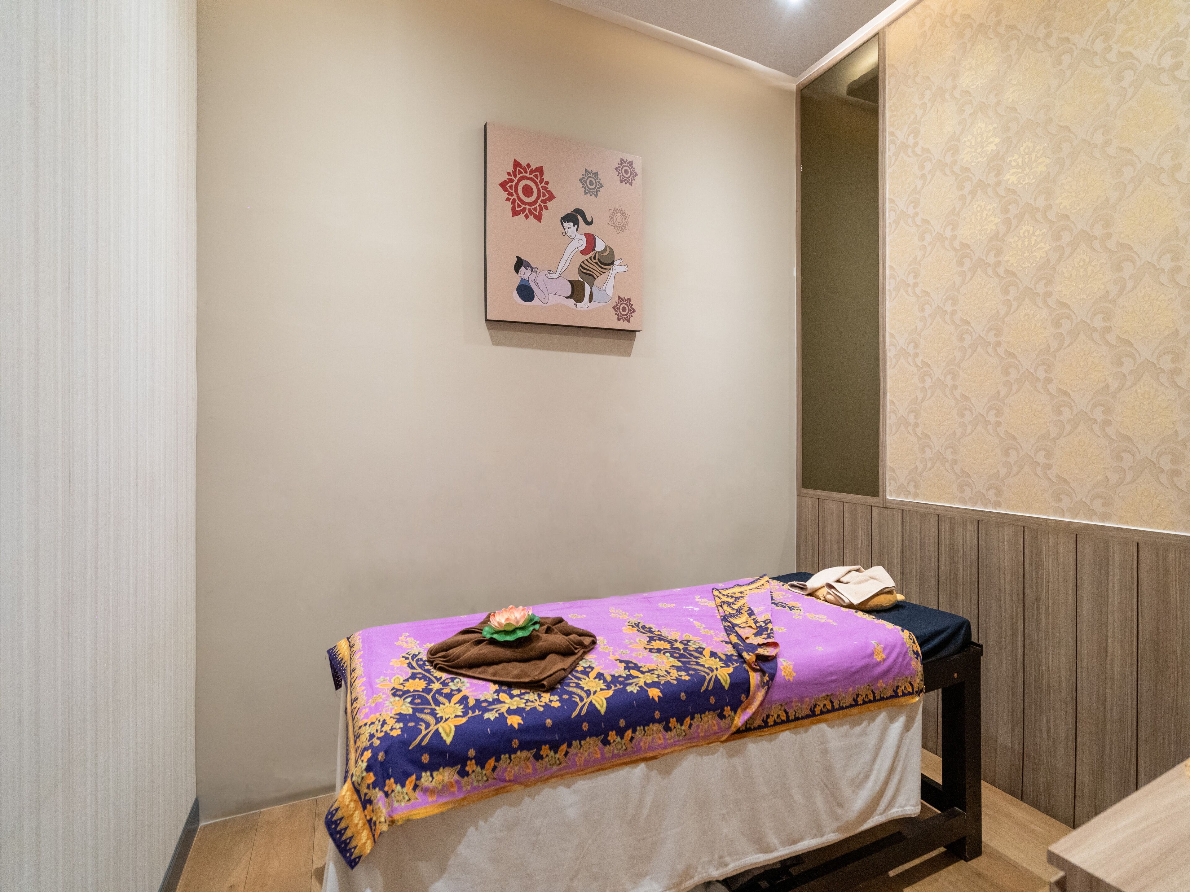 A massage table with a purple and gold blanket, a towel, and a lotus flower decoration.