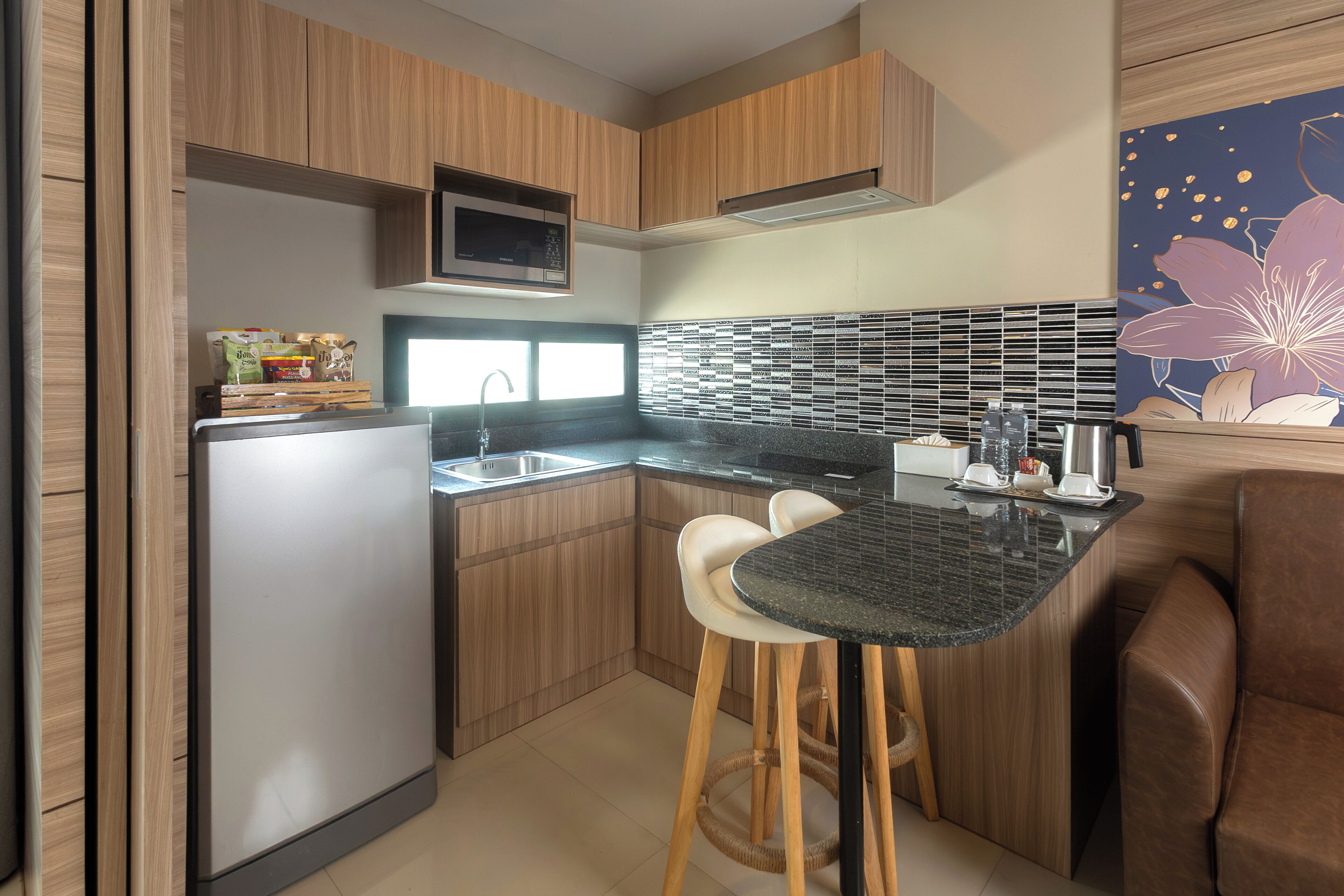 A compact kitchen with wooden cabinets, a built-in microwave, a sink, and a small dining area with stools.