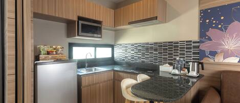 A compact kitchen with wooden cabinets, a built-in microwave, a sink, and a small dining area with stools.