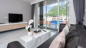 A modern living room with a large TV, comfortable seating, a marble coffee table, and a view of a cityscape through large windows. - Patong Bay Residence  (Patong)