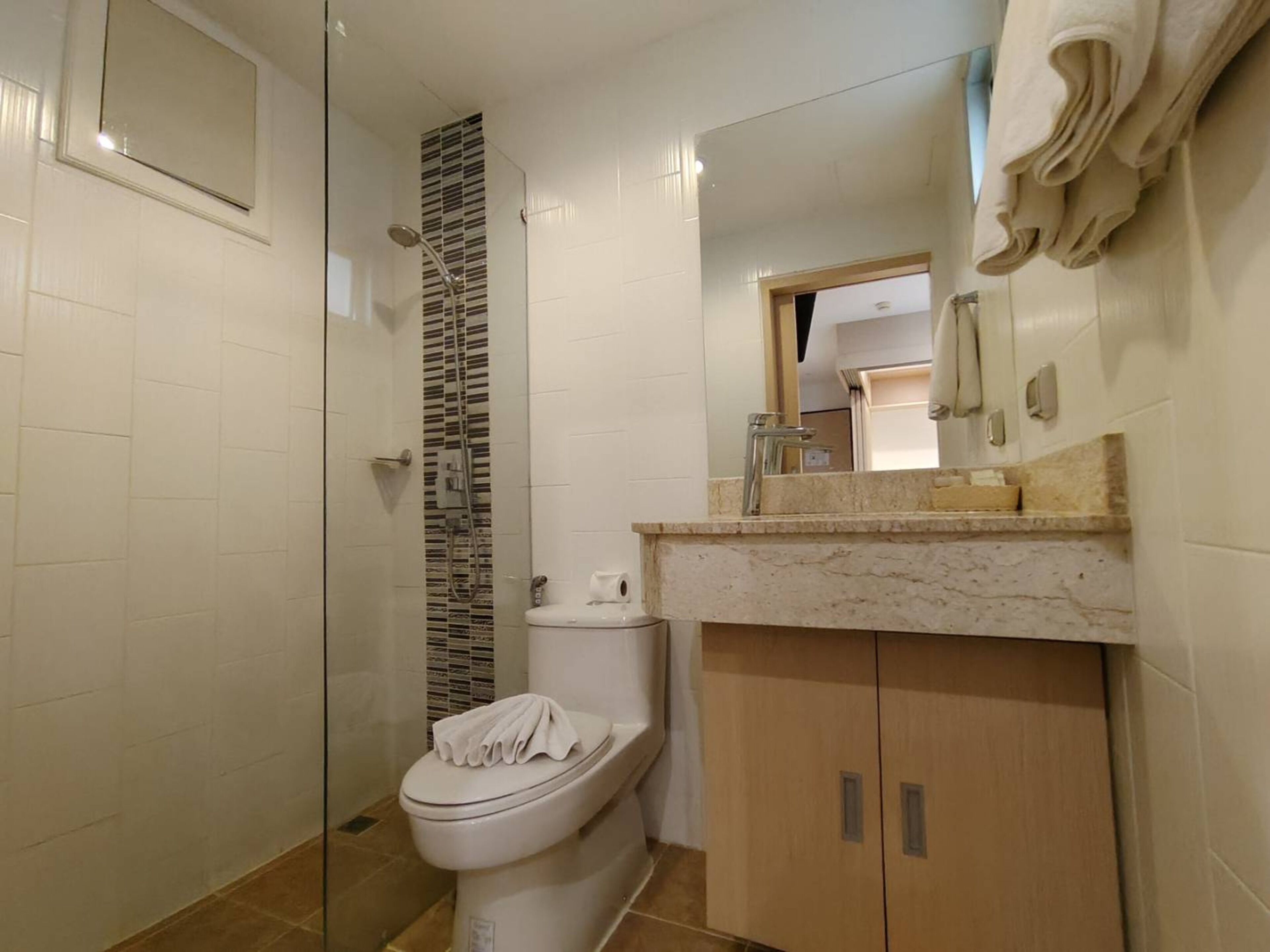 A bathroom with a glass shower enclosure, a toilet, a sink with a marble countertop, and a wooden cabinet.