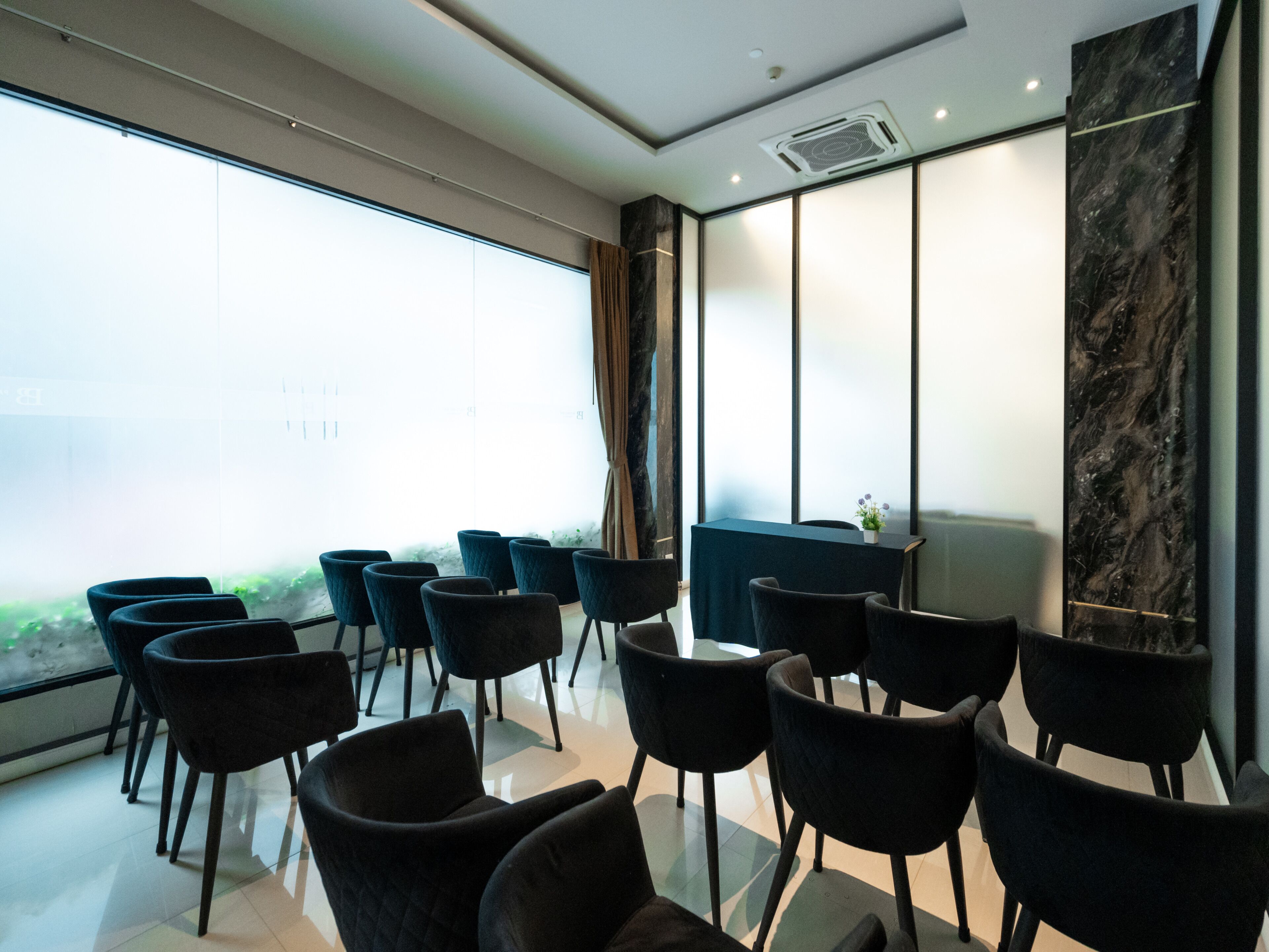 A modern conference room with a long table and several chairs, large windows with a view, and a marble accent wall.