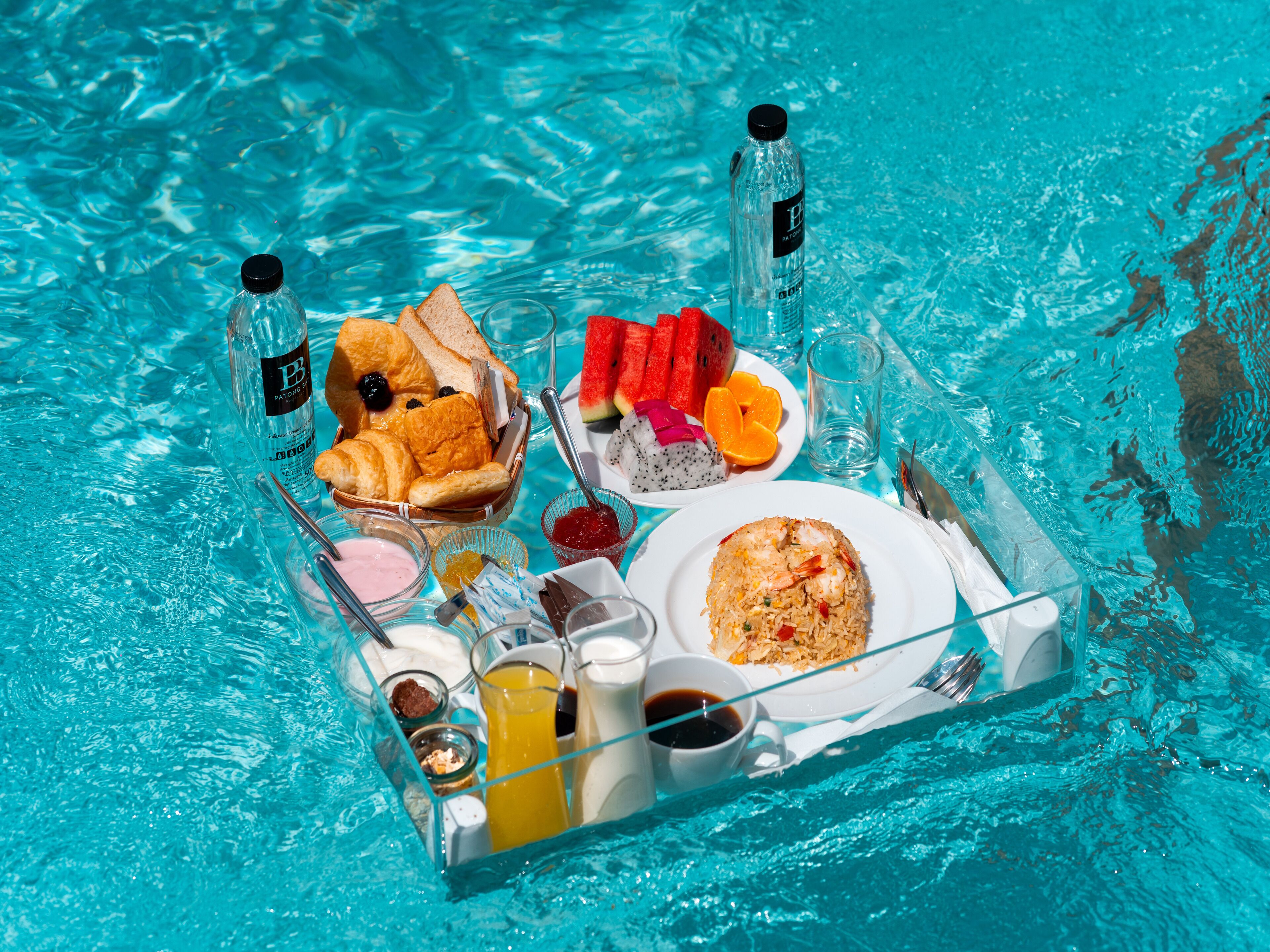 Ett brickbord med croissanter, frukt och en tallrik med stekt ris, som flyter på en pool.
