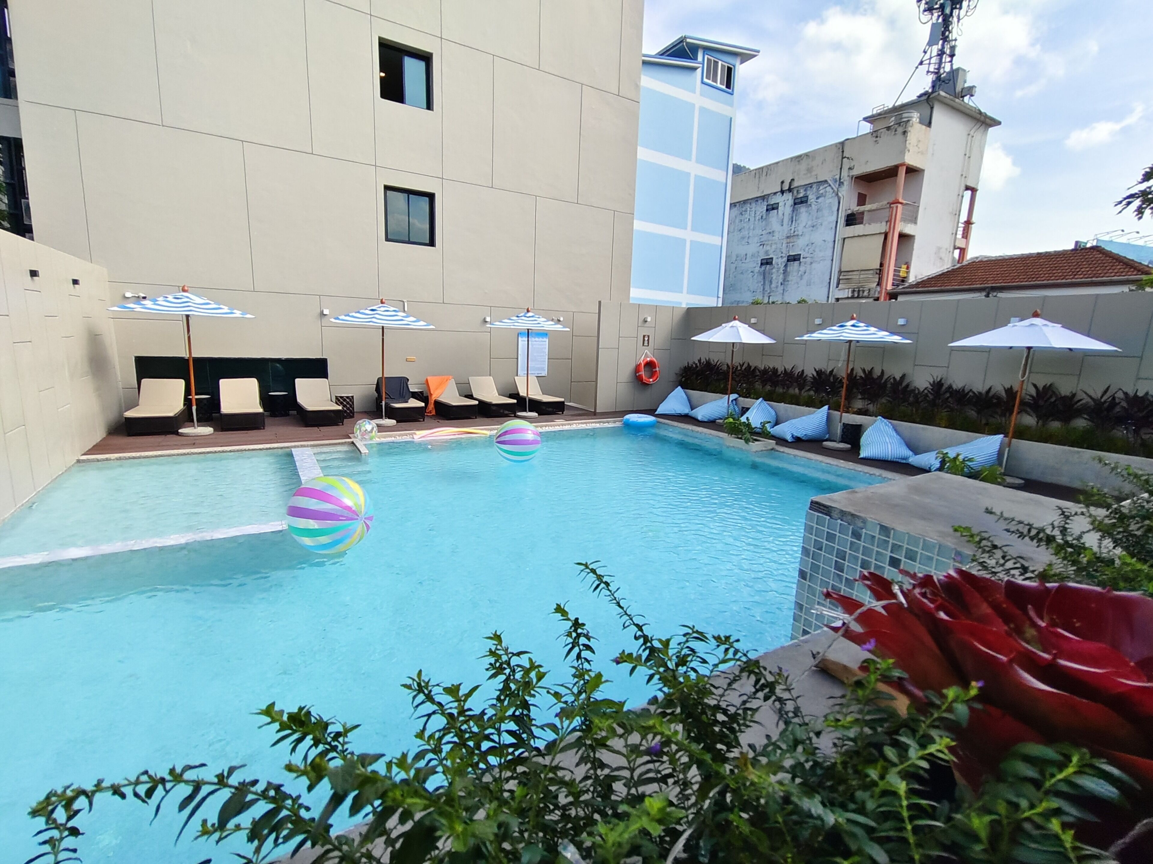 A swimming pool with lounge chairs and umbrellas, surrounded by a building with a tiled exterior.