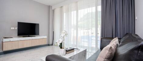 Una sala de estar moderna con un televisor de pantalla plana, una mesa de centro de mármol, un sofá de cuero y un amplio ventanal con cortinas translúcidas.