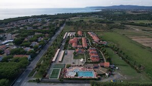 Ein Luftbild eines Resorts mit Schwimmbad, Tennisplatz und einer entlangführenden Straße.