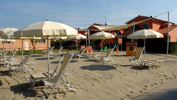 Relax on the beach with comfortable sun loungers and umbrellas, surrounded by Mediterranean-style buildings.
