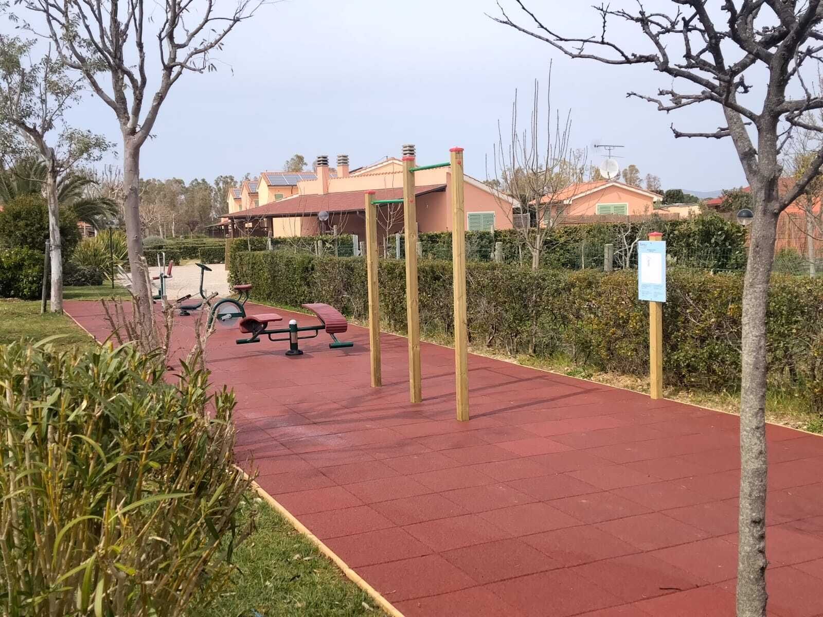 A red-tiled pathway with exercise equipment, surrounded by greenery and buildings.