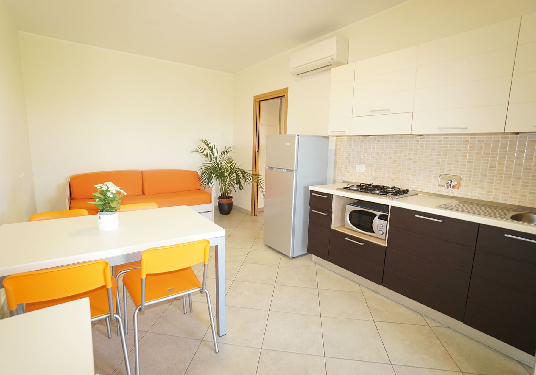 A compact kitchen with a refrigerator, stove, microwave, and a sink. There is a dining area with a table and chairs.
