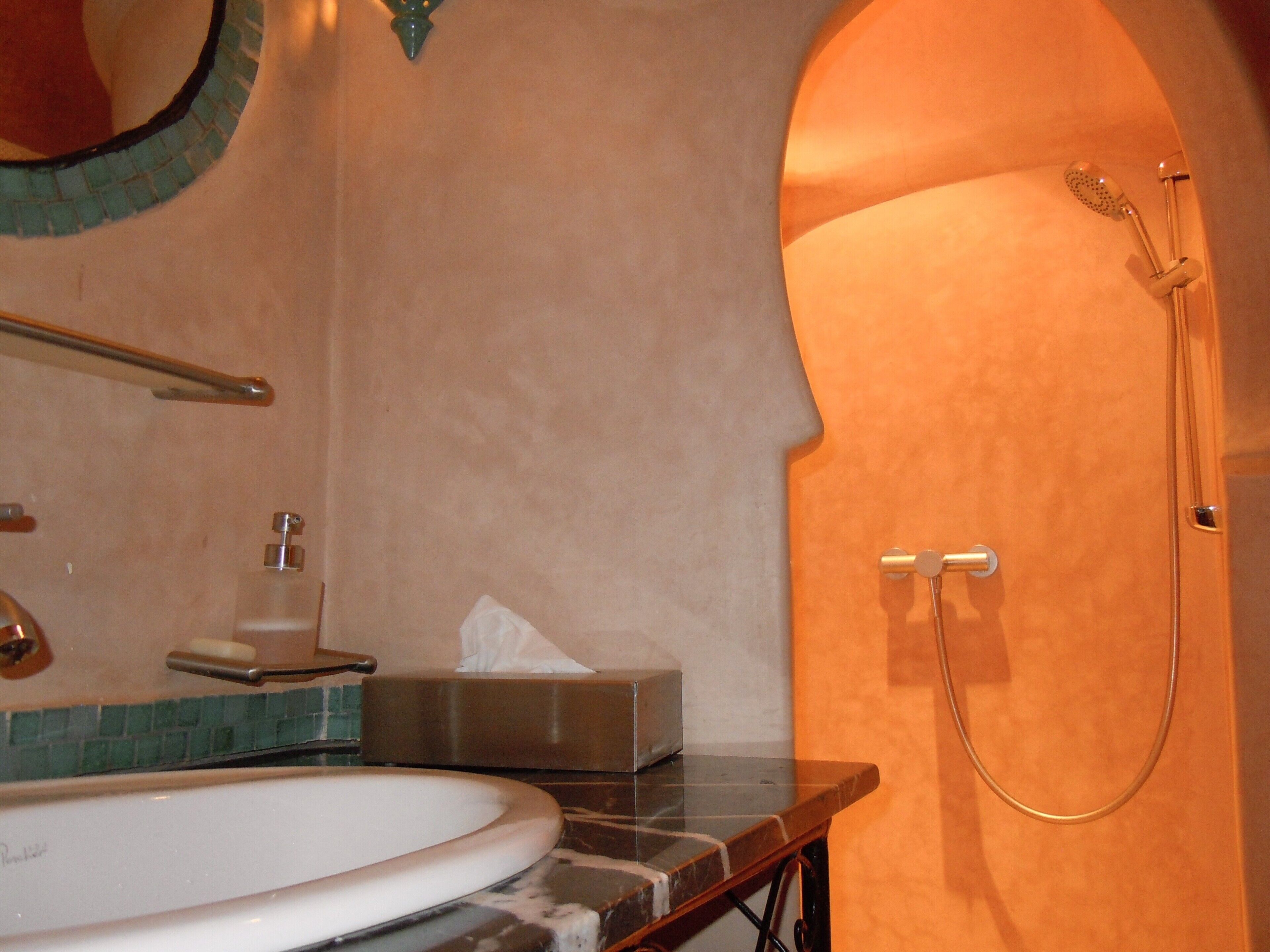 Un baño con lavamanos de mármol, espejo, toallero, ducha y caja de pañuelos.