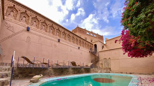 Una piscina con borde de azulejos, una escultura de piedra y una escalera que conduce a un edificio con elaboradas esculturas en la pared.
