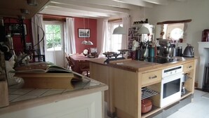 Een keuken met een houten kookeiland, witte apparaten en een eetgedeelte met een rode muur en gordijnen.