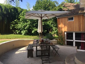 Un área de comedor al aire libre con mesa de madera, bancos y una sombrilla grande.