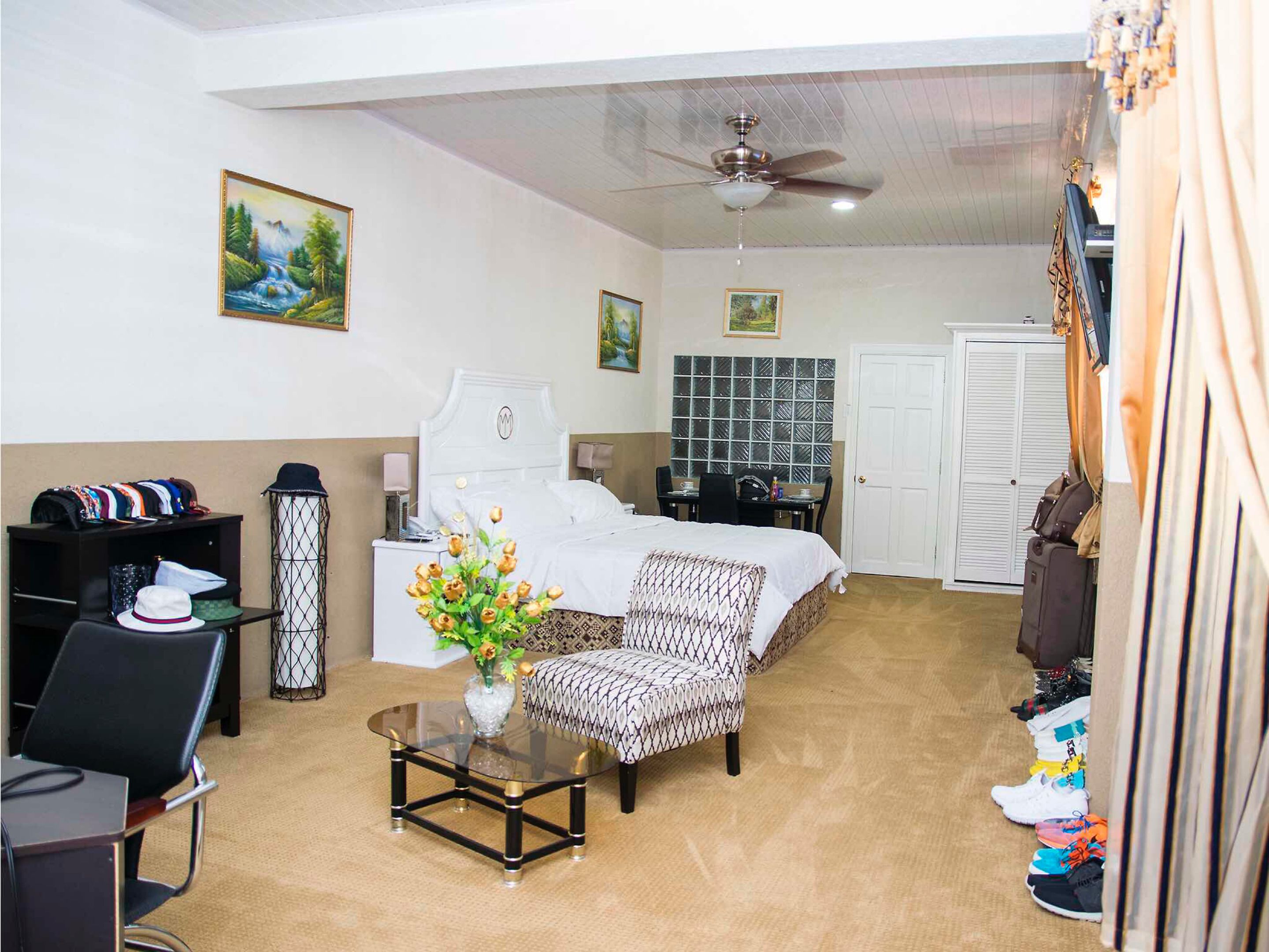 A hotel room with a bed, a desk, a chair, a glass coffee table, a wardrobe, and a ceiling fan.