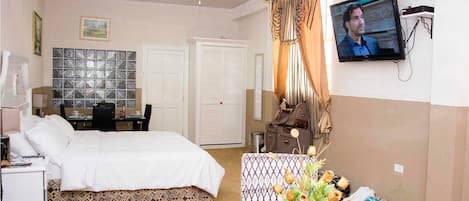 A hotel room with a bed, a desk with a chair, a television, a wardrobe, and a window with blinds.