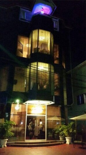 A multi-story building with a glass facade, a covered entrance, and potted plants around the entrance.