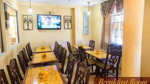 A breakfast room with multiple tables and chairs, a television, and decorative wall pieces. - Millenium Manor Hotel (Georgetown)