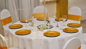 A round table set for a formal event with white and gold tableware, clear glassware, and a central decorative piece. - Millenium Manor Hotel (Georgetown)