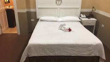 A hotel room with a neatly made bed, a bedside table with a lamp, a phone, and a sign that says "Welcome".