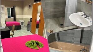 A hotel room with a bed, a desk, a chair, a wardrobe, a television, a bathroom with a sink, a bathtub, and a shower. - Millenium Manor Hotel (Georgetown)