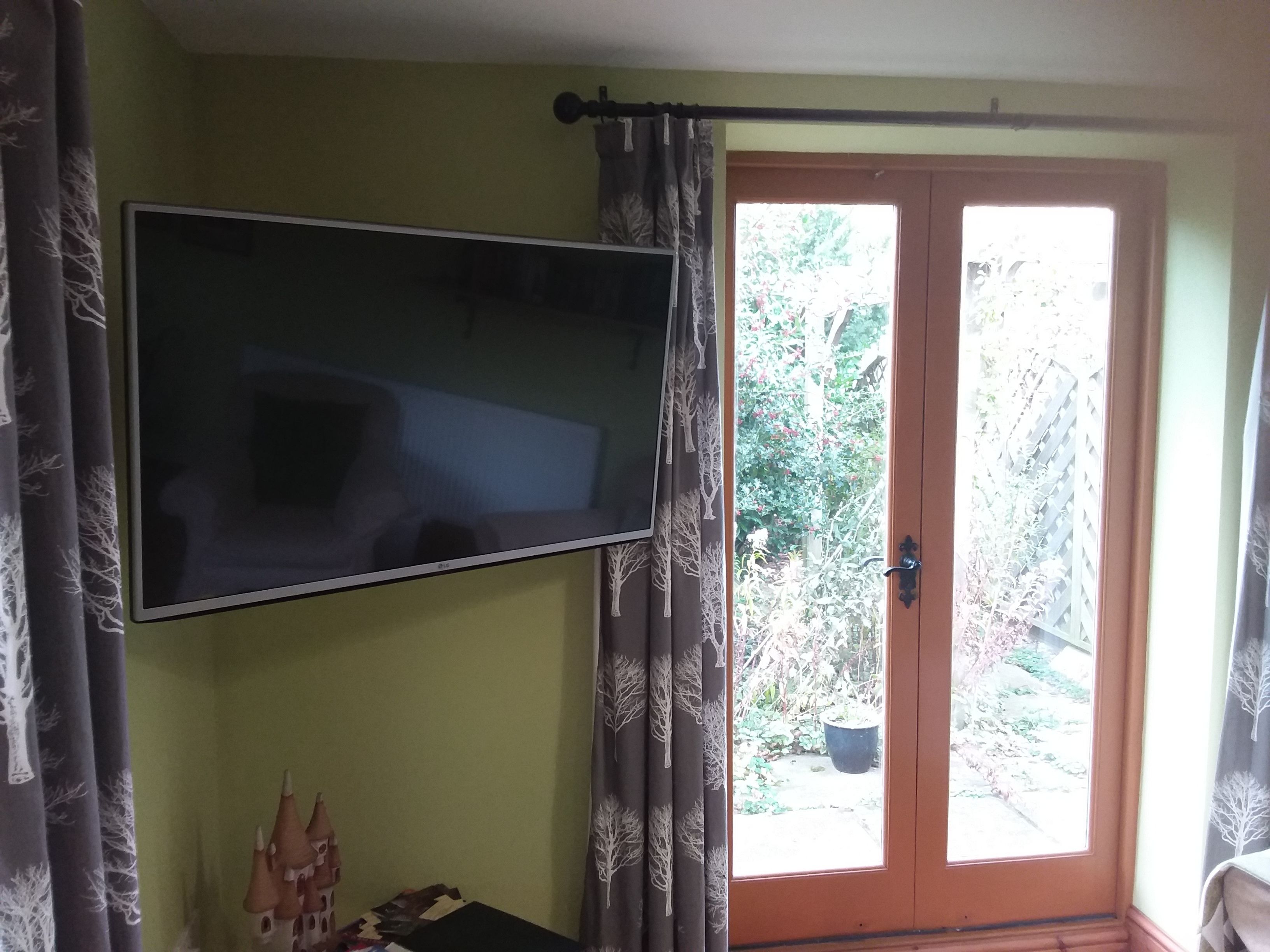 A room with a flat-screen TV mounted on the wall, a door leading to a garden, and a small castle model on a table.