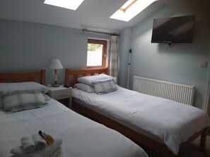 A hotel room with two single beds, a TV mounted on the wall, a window with curtains, and a skylight. - Field View B&B (Goole)